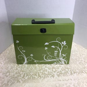 May include: A rectangular olive green storage box with a glossy finish, featuring a black plastic handle on top and a black latch closure. The front of the box is decorated with a white printed design of swirling vines and small leaves.
