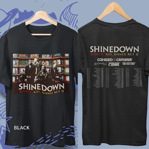 以下が含まれることがあります： テレビ画面の前に立つバンドShinedownと「Shinedown Dance, Kid, Dance Act II」の文字がプリントされた黒いTシャツ。背面にはツアー日程とCoheed and Cambriaを含む出演バンド名が記載されています。