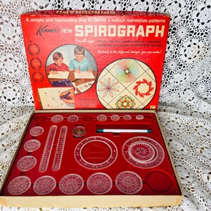 May include: Vintage Spirograph set in a red box. The box reads "A simple and fascinating way to DRAW a million marvelous patterns." The set includes clear plastic gears, rulers, and a pen, all arranged on a red velvet-lined tray. The box is open, revealing the contents.