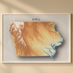 Puede incluir: Impresión artística enmarcada del mapa del estado de Iowa. El mapa presenta un diseño topográfico 3D con tonos marrones, beige y azules, sobre un fondo neutro. La palabra "IOWA" está impresa en la parte superior del marco.
