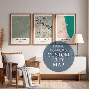 May include: Three framed city maps, featuring Nashville, Amsterdam, and Chicago, in a modern interior setting. The maps have a minimalist design with muted color palettes. A digital download custom city map is advertised. A chair, blanket, and lamp are also visible.