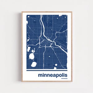 Puede incluir: Una impresión enmarcada que presenta un mapa detallado de Minneapolis en azul marino y blanco. El diseño de la ciudad, incluyendo calles y vías fluviales, es claramente visible. La palabra "minneapolis" está impresa en negrita en la parte inferior.