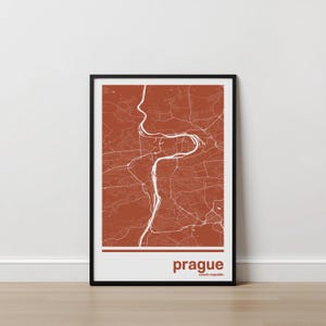May include: Framed map print of Prague, Czech Republic. The map features a detailed white outline of the city's streets and river on a terracotta background. The word "prague" is printed in a brown font at the bottom of the print.