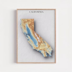 Puede incluir: Impresión enmarcada que presenta un mapa topográfico 3D de California. El mapa utiliza tonos de azul, marrón y dorado para representar el terreno del estado. La palabra "CALIFORNIA" está impresa en negro en la parte superior del marco.