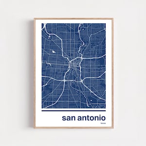 Puede incluir: Una impresión enmarcada de un mapa de San Antonio, Texas, en un estilo minimalista. El mapa presenta líneas blancas sobre un fondo azul oscuro, que representan las calles y vías fluviales de la ciudad. El nombre de la ciudad está impreso en blanco en la parte inferior, con "texas" debajo.