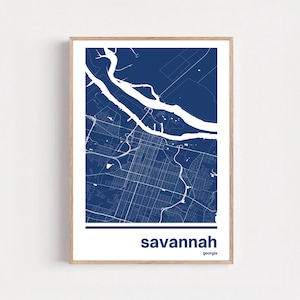 May include: A framed print featuring a detailed map of Savannah, Georgia, in a navy blue and white color scheme. The city's layout is depicted with streets and waterways. The word "savannah" is printed in a bold, sans-serif font below the map, with "georgia" in a smaller font.