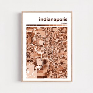 May include: A framed print featuring a map of Indianapolis, Indiana. The map is rendered in shades of brown and beige, with the city name and state displayed at the top. The frame is a light wood color.