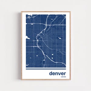 May include: A framed print featuring a detailed map of Denver, Colorado, in a navy blue and white color scheme. The city's layout is depicted with intricate road and waterway details. The word "denver" is printed in white at the bottom.