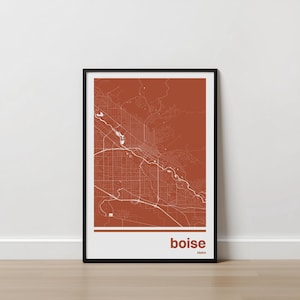 May include: Framed map print of Boise, Idaho, in a minimalist style. The map features white lines against a terracotta background, with the city name and state at the bottom. The print is encased in a black frame.