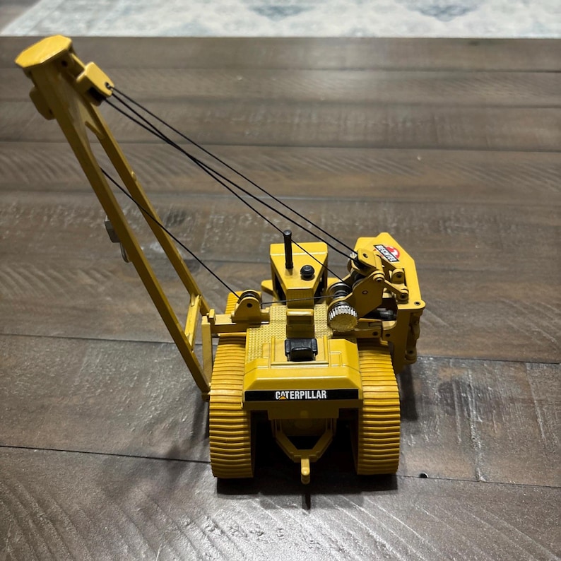 Pu&ograve; includere: Un modellino di gru Caterpillar giallo con cingoli neri, un braccio sollevato e sottili cavi di sollevamento neri. Il veicolo da cantiere presenta una cabina operatore dettagliata, un piccolo scarico nero e il logo Caterpillar stampato sul retro.