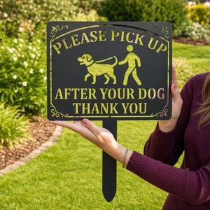 Könnte beinhalten: Ein schwarzes Metallschild für den Garten mit einem Scherenschnitt-Design einer Person, die einen Hund ausführt. Der Text lautet: PLEASE PICK UP AFTER YOUR DOG THANK YOU. Das Schild hat dekorative Schnörkel an den Ecken und einen Erdspieß.