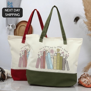 May include: Two canvas tote bags with the text "it's a good day to read a book" and a graphic of books and flowers. One bag has a red base and handles, the other has a green base and handles. Both bags are off-white.