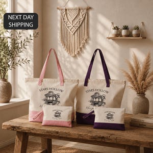 a set of four tote bags with the text "STARS HOLLOW" printed on them, placed on a wooden table. The bags are accompanied by a small bag and a larger bag, all of which are white. The setting includes a window, a wall with a hanging decoration, and some potted plants. The image also includes text that reads "NEXT DAY SHIPPING".