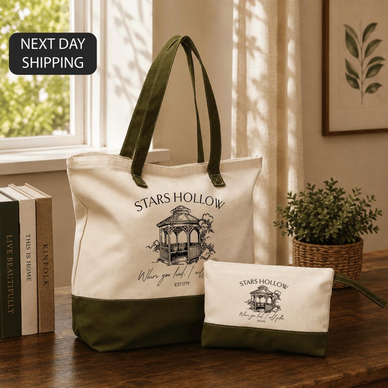 a large tote bag with a printed design and text, placed on a wooden surface next to a small bag, with a plant and books in the background.