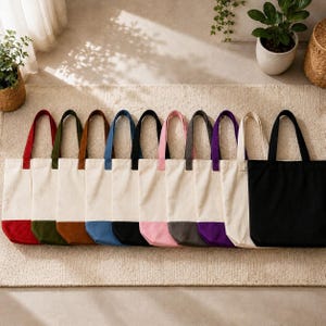A row of colorful tote bags with various patterns and colors, including white, black, and multicolored designs, neatly arranged on a beige rug.