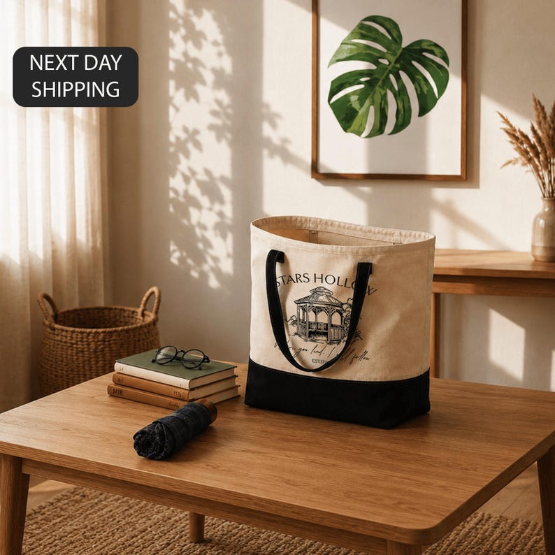 a wooden coffee table with a tote bag, a stack of books, a folded blue shirt, and a framed plant on the wall.