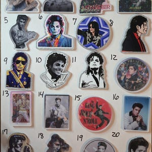 May include: A collection of twenty acrylic pins featuring portraits and illustrations of Justin Bieber, Michael Jackson, and Elvis Presley. The pins vary in shape, including circular and die-cut designs, with some featuring text like The King of Rock N' Roll.