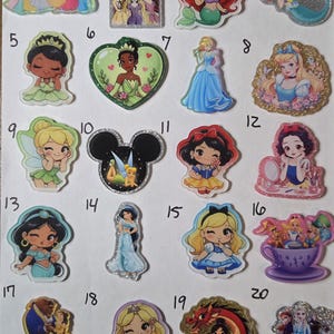 May include: A collection of twenty numbered acrylic pins featuring various animated characters. The designs include chibi-style figures, princesses, and scenes with glitter accents, all arranged in a grid on a plain white background.