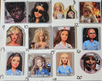 May include: A collection of twenty square and shaped acrylic pins featuring various doll faces with diverse expressions, hairstyles, and outfits, including some with text such as 'absolutely not' and 'sorry I'm not perfect' on a white background.