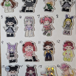 May include: A collection of sixteen individual acrylic character charms arranged in a grid, each numbered one through sixteen. The charms feature diverse illustrated figures in various outfits, including anime-inspired designs, animal-themed costumes, and colorful accessories, with one holographic charm.