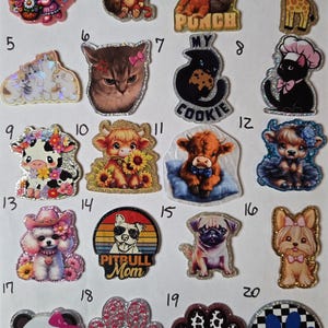 May include: A collection of twenty numbered acrylic charms featuring various illustrations including animals like cats, dogs, cows, a giraffe, and monkeys, alongside paw prints and text such as Team Punch, My Cookie, and Pitbull Mom with glittery edges.