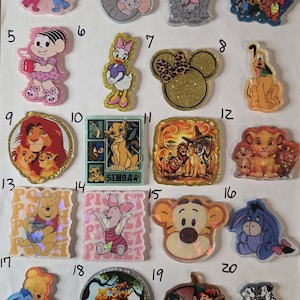 May include: A collection of twenty numbered acrylic character charms featuring various animated figures including Blue, Dumbo, Daisy Duck, Mickey Mouse ears, Pluto, Simba, The Lion King, Winnie the Pooh, Piglet, Tigger, Eeyore, Peter Pan, and Dalmatians.