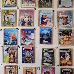 May include: A collection of twenty rectangular magnets featuring various Disney movie posters and Garbage Pail Kids trading card illustrations, each framed with a gold glitter border and numbered from one to twenty on a white background.