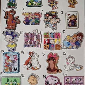 May include: A collection of twenty numbered acrylic pins featuring various cartoon characters from Rugrats, Disney films, VeggieTales, and Peanuts. The pins include individual characters, group scenes, and the text 90's BABY, all with glittery finishes.