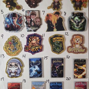 May include: A collection of twenty numbered acrylic pins featuring Harry Potter characters, house crests, and book covers. The designs include chibi-style figures, magical scenes, and rectangular book covers with glittery borders and holographic finishes.