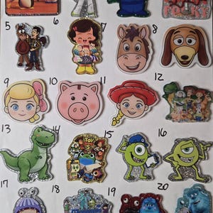 May include: A collection of twenty glittery acrylic character charms featuring various animated figures from Toy Story and Monsters Inc. Each charm is numbered and displays colorful illustrations of characters like Buzz Lightyear, Woody, Mike Wazowski, and Sulley.