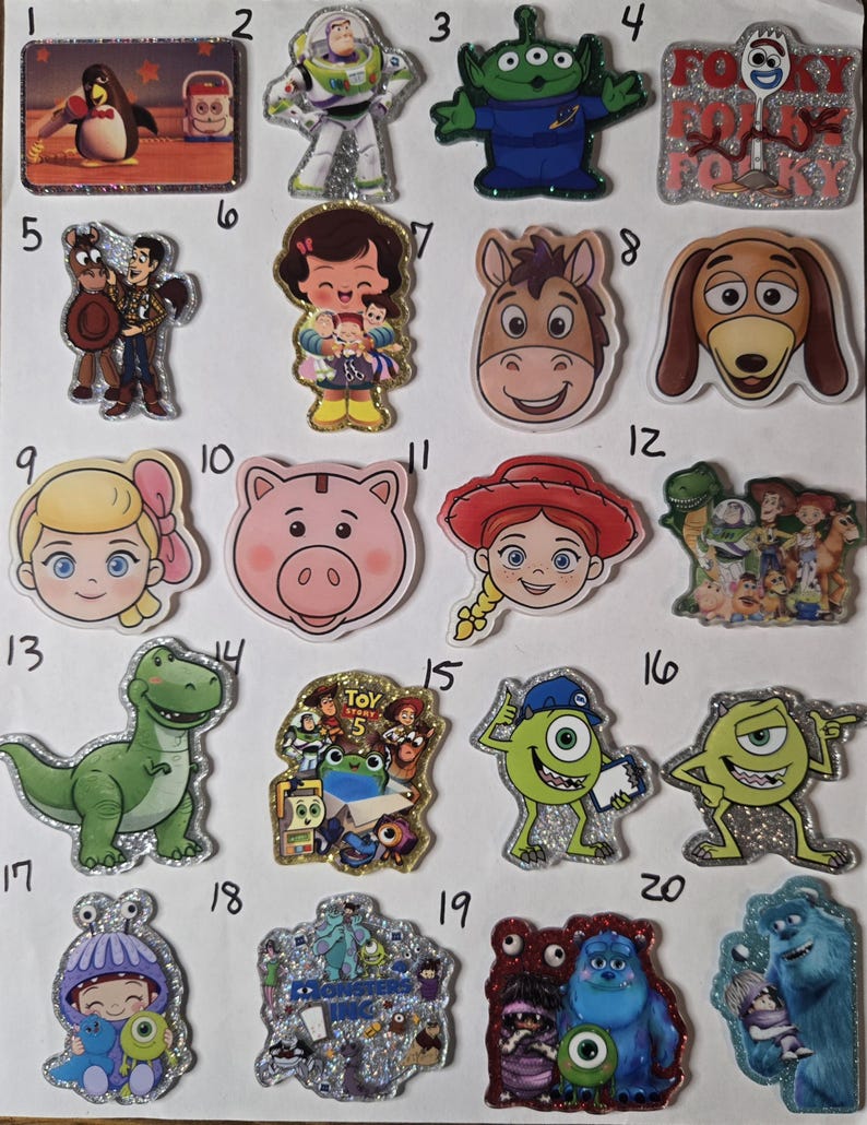 May include: A collection of twenty glittery acrylic character charms featuring various animated figures from Toy Story and Monsters Inc. Each charm is numbered and displays colorful illustrations of characters like Buzz Lightyear, Woody, Mike Wazowski, and Sulley.