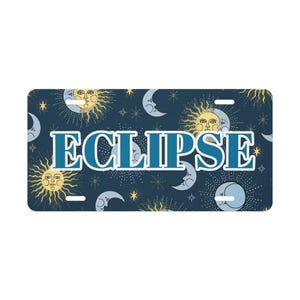 May include: A rectangular license plate with a navy blue background featuring a celestial pattern of suns, moons, and stars. The word "ECLIPSE" is displayed in large, teal letters across the centre.