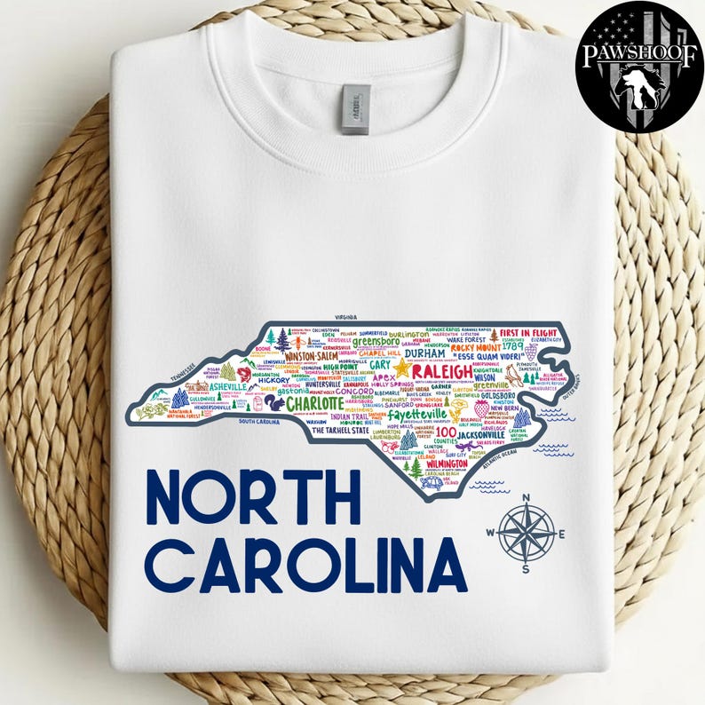 Puede incluir: Sudadera blanca con un mapa detallado de Carolina del Norte, lleno de nombres de ciudades y puntos de referencia. Las palabras "NORTH CAROLINA" est&aacute;n impresas en azul marino debajo. Tambi&eacute;n se incluye una rosa de los vientos.