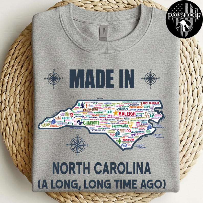 May include: A grey sweatshirt featuring the text "MADE IN NORTH CAROLINA (A LONG, LONG TIME AGO)". The design includes a map of North Carolina with city names and compass graphics.