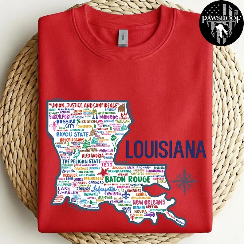 May include: A red sweatshirt featuring a detailed map of Louisiana, with city names and the state outline in white and blue. The text "LOUISIANA" is in large blue letters, and the state motto is at the top. A PawShoof logo is in the upper right corner.