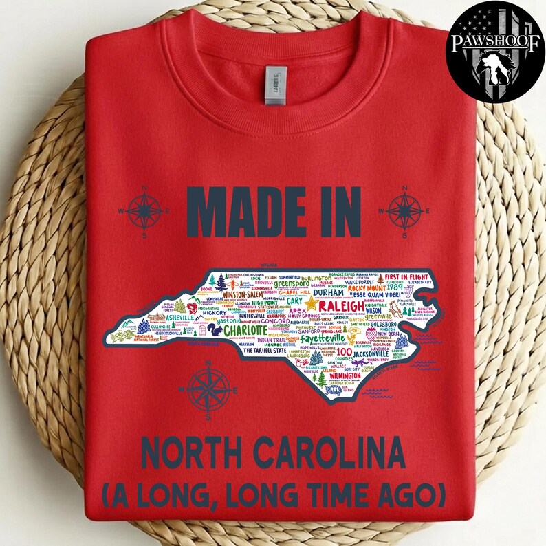 May include: Red sweatshirt featuring the text "MADE IN NORTH CAROLINA" and a map of North Carolina filled with city names. The phrase "A LONG, LONG TIME AGO" is also present. Compass rose designs are included.