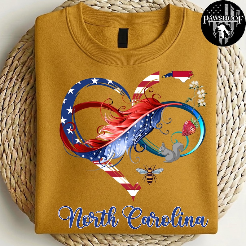 May include: A mustard yellow crewneck sweatshirt featuring a graphic of an infinity heart shape with red, white, and blue stripes and stars. The design includes a North Carolina state outline, a strawberry, a squirrel, a bee, and the text North Carolina.