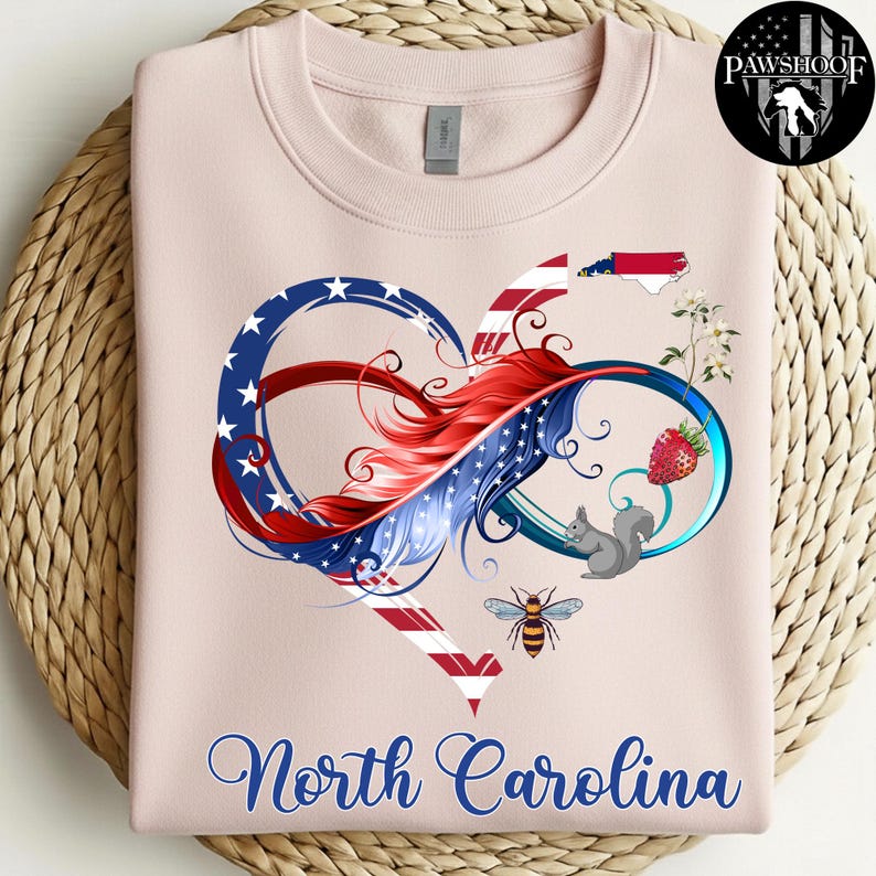 May include: A light pink crewneck sweatshirt featuring a graphic of an infinity heart symbol colored with red, white, and blue stars and stripes. The design includes a North Carolina state map, a strawberry, a squirrel, a bee, and flowers.