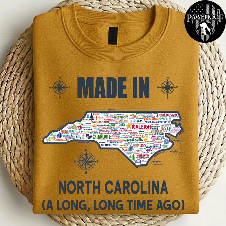 May include: Mustard-coloured sweatshirt with the text "MADE IN NORTH CAROLINA (A LONG, LONG TIME AGO)". The design includes a map of North Carolina with city names and compass rose graphics.