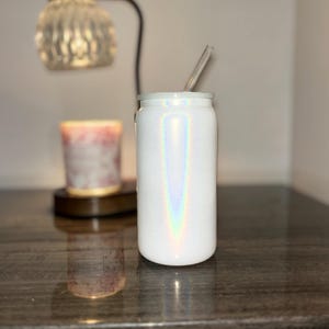 K&ouml;nnte beinhalten: Wei&szlig;er, schillernder Becher mit einem durchsichtigen Strohhalm. Der Becher hat eine zylindrische Form mit einem wei&szlig;en Deckel. Die schillernde Oberfl&auml;che erzeugt einen Regenbogeneffekt. Ein klarer Glasstrohhalm ist in den Deckel eingesetzt.