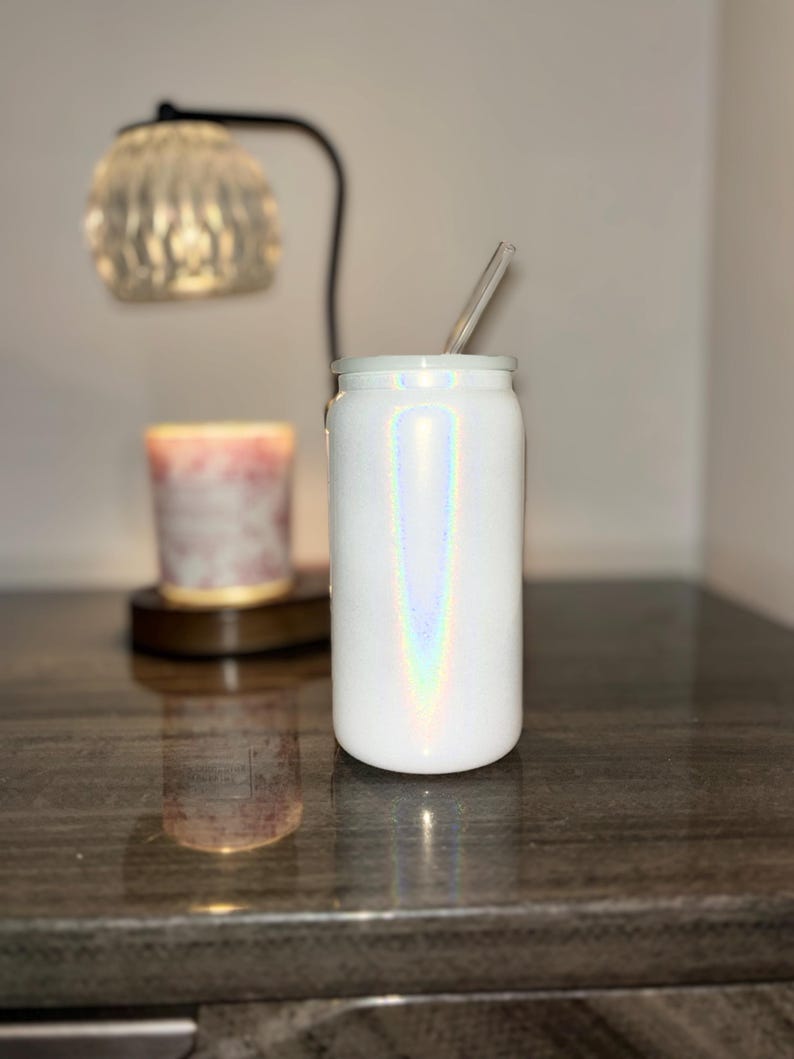 K&ouml;nnte beinhalten: Wei&szlig;er, schillernder Becher mit einem durchsichtigen Strohhalm. Der Becher hat eine zylindrische Form mit einem wei&szlig;en Deckel. Die schillernde Oberfl&auml;che erzeugt einen Regenbogeneffekt. Ein klarer Glasstrohhalm ist in den Deckel eingesetzt.
