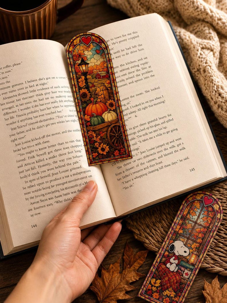 An autumn-themed stained-glass bookmark rests on an open book with another bookmark visible below it.