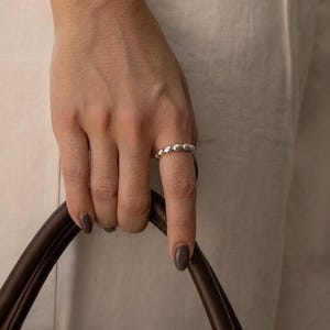 Puede incluir: Un anillo de plata que presenta una banda continua de pequeñas cuentas metálicas redondeadas y pulidas. El anillo tiene una superficie lisa y reflectante con una forma circular uniforme, diseñado para llevarse en el dedo como accesorio.