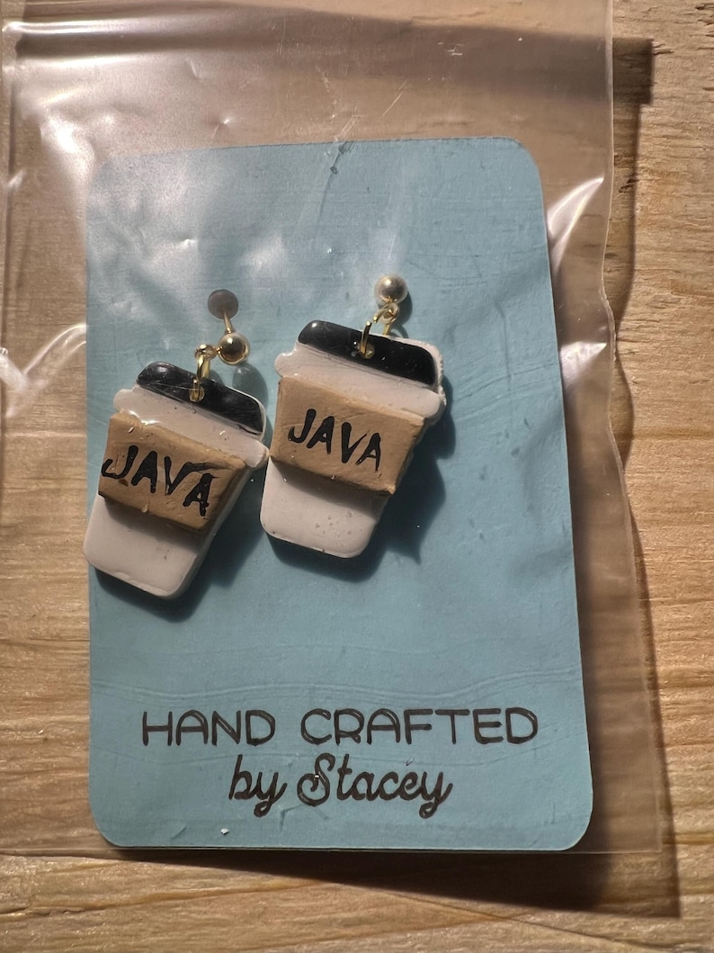 Peut inclure: Boucles d'oreilles faites &agrave; la main en forme de tasses &agrave; caf&eacute;. Chaque boucle d'oreille est une r&eacute;plique miniature d'une tasse &agrave; caf&eacute;, avec un couvercle noir, une tasse blanche et une bande marron avec le mot "JAVA".