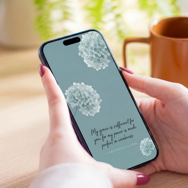 Puede incluir: Un tel&eacute;fono inteligente que muestra un fondo de pantalla digital con un fondo azul verdoso apagado, tres racimos de flores de hortensia azul claro y el texto negro: My grace is sufficient for you, for my power is made perfect in weakness. 2 Corinthians 12:9 WEB.