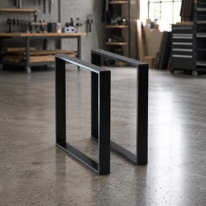 May include: Two rectangular furniture legs constructed from matte black metal tubing. Each leg features a continuous square frame design with clean, sharp corners and a smooth finish, standing upright as a pair for table or bench support.
