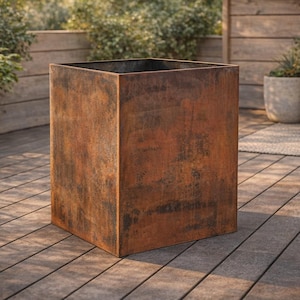 May include: A large, square, outdoor planter with a weathered, rust-colored finish. The planter is made of metal and has a simple, modern design. It is sitting on a wooden deck, with plants and outdoor furniture in the background.