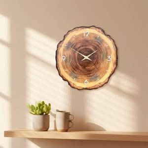 May include: A round wooden wall clock with a natural wood grain pattern. The clock face features white numerals at the 12, 3, 6, and 9 o'clock positions, and gold-colored hands. The clock is approximately 12 inches in diameter.