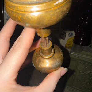 May include: A vintage brass door knob set featuring two spherical knobs connected by a central threaded metal spindle. The brass surface shows signs of age, including a dull patina and minor surface wear, with a smooth, rounded shape for each knob.