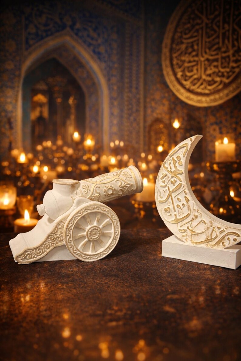 Puede incluir: Una escultura decorativa blanca de un ca&ntilde;&oacute;n y una luna creciente con detalles dorados. El ca&ntilde;&oacute;n tiene detalles de volutas y una rueda. La luna presenta caligraf&iacute;a &aacute;rabe. El fondo incluye velas y un arco ornamentado.